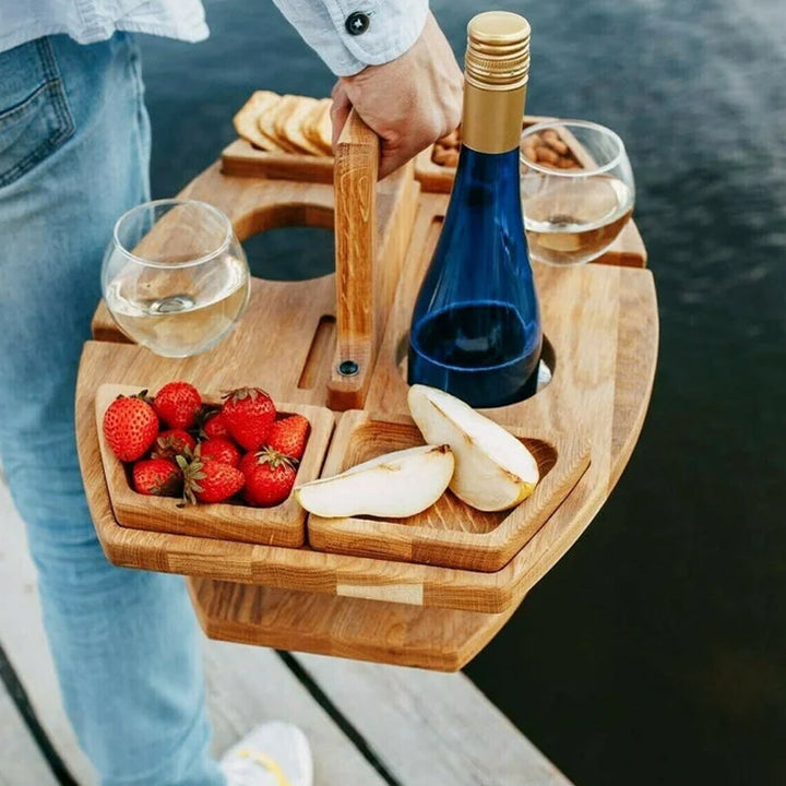 Draagbare houten picknicktafel met handvat, wijnfles, glazen, aardbeien en peer.
