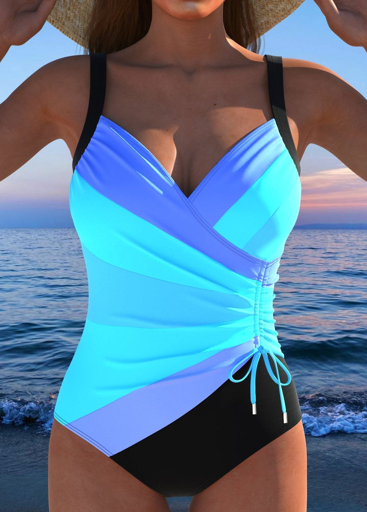 Dames badpak in blauwtinten met diagonale strepen en wrap-effect bij de borst, bij zonsondergang.