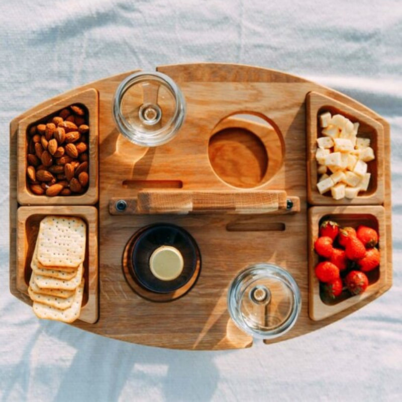 Bovenaanzicht van houten picknicktafel gevuld met glazen, nootjes, aardbeien en kaasjes.