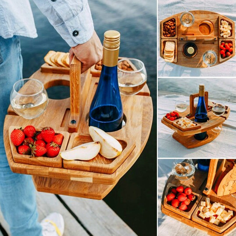 Pers draagt houten picknicktafel met wijn, fruit en snacks aan een meer, genietend van de natuur.