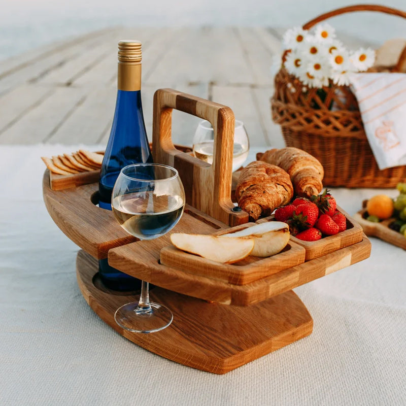 Opvouwbare houten picknicktafel met wijnfles, glas, croissants en aardbeien, op een lichte achtergrond.