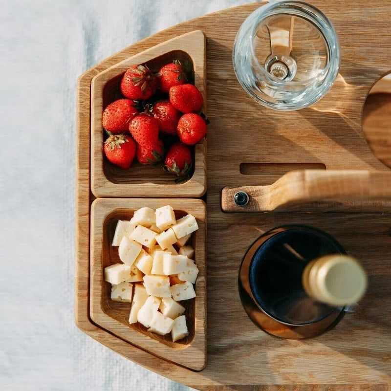 Houten picknicktafel met weinflasche, glazen, aardbeien en kaasblokjes, perfect voor buitenactiviteiten.