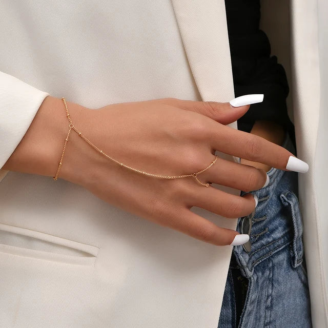 Vrouwenhand met elegante goudkleurige Aurelia handketting op een witte blazer en spijkerbroek.