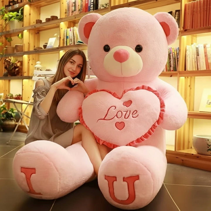 Grote pluche teddybeer in roze kleur, meisje zit ernaast in een sfeervolle kamer.