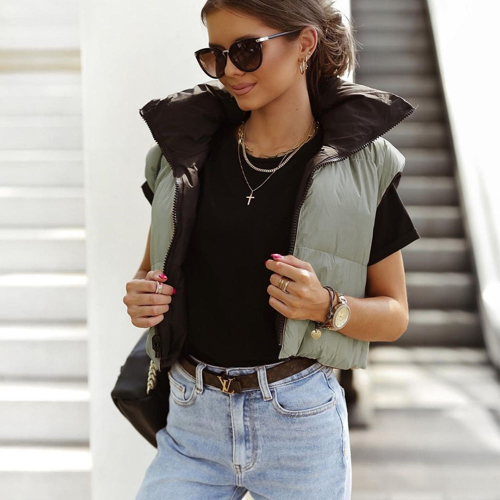 Dames draagt een korte dubbelzijdige bodywarmer in groen en zwart met zonnebril en accessoires