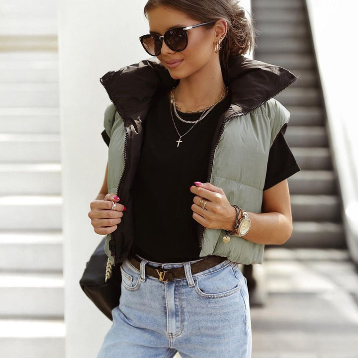 Dames draagt een korte dubbelzijdige bodywarmer in groen en zwart met zonnebril en accessoires