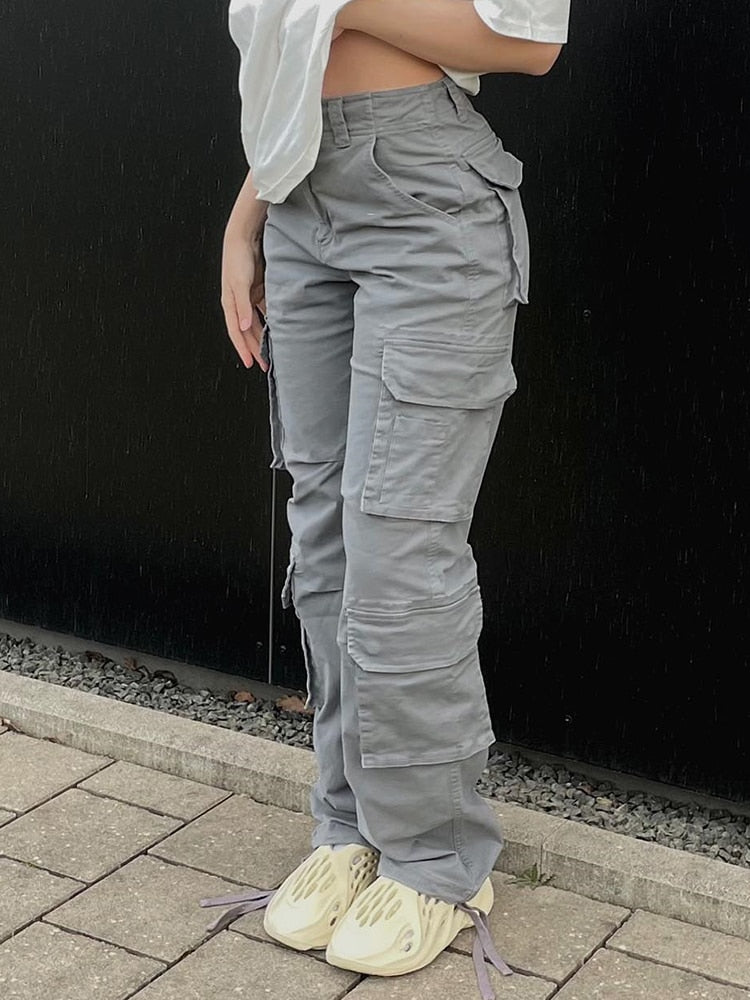Vrouw in een donkere cargobroek met wijde pijpen, staand met een hand in haar zak, focus op de broek.