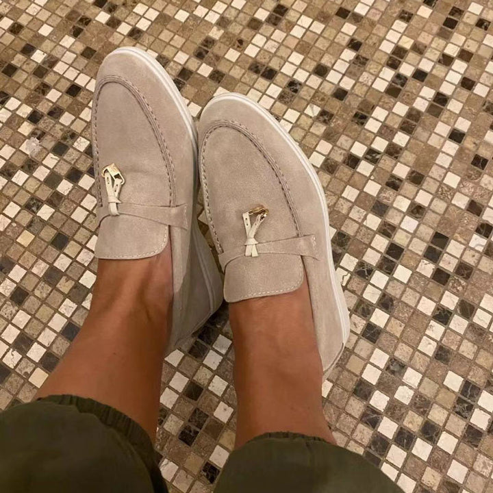 Beige dames loafers met gepunte neus en gouden detail gedragen op een tegelvloer