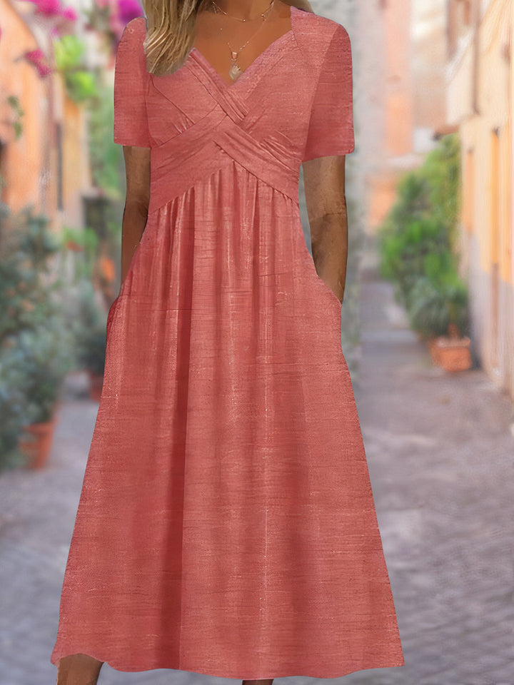 Model draagt een lichte zomerjurk met geplooide taille en v-hals, staand in een steegje