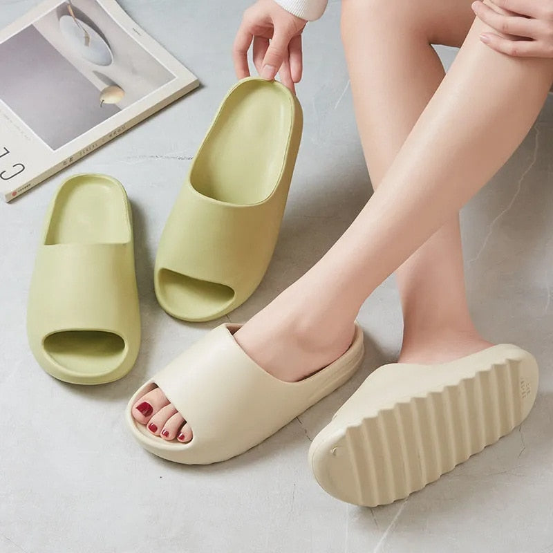 Vrouwenvoeten met beige ElliesSlippers en een groene slipper ernaast