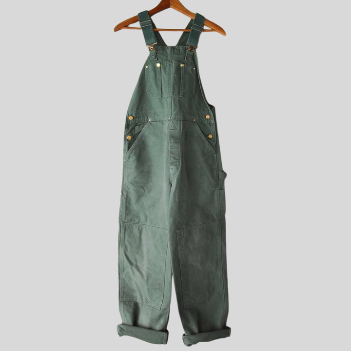 Dames retro tuinbroek in stijlvolle groene kleur hangend aan een houten hanger, met verstelbare bandjes en functionele zakken