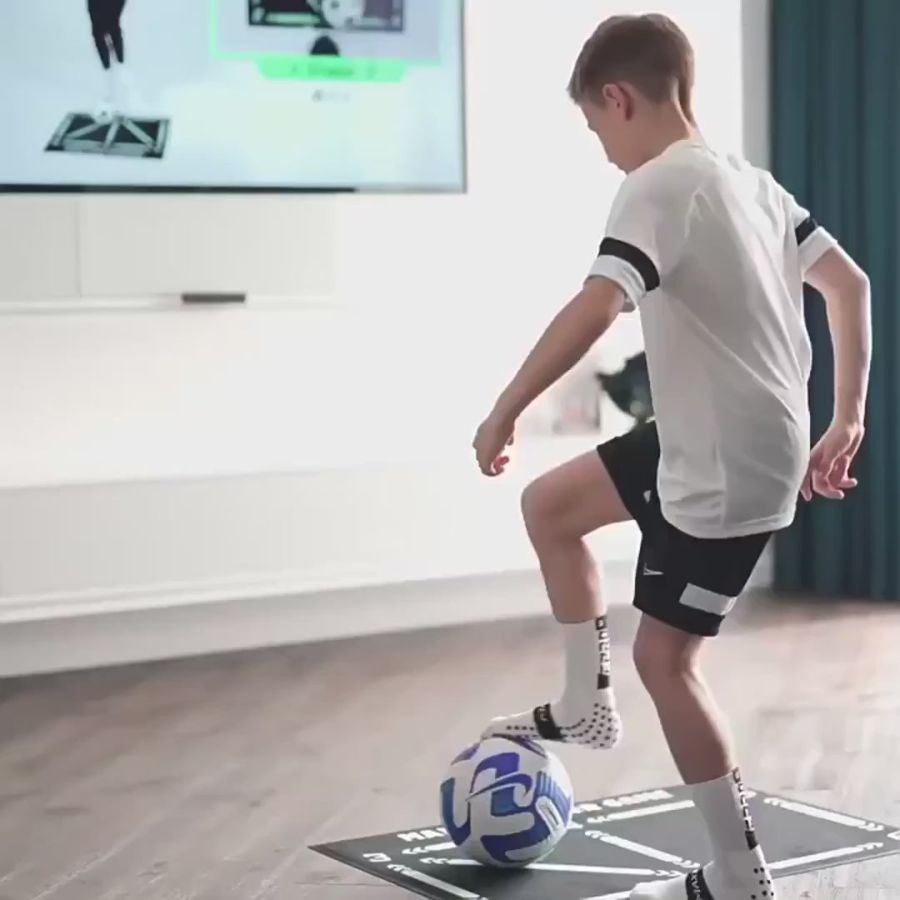 Jonge voetballer traint thuis balcontrole op de trainingsmat voor de televisie