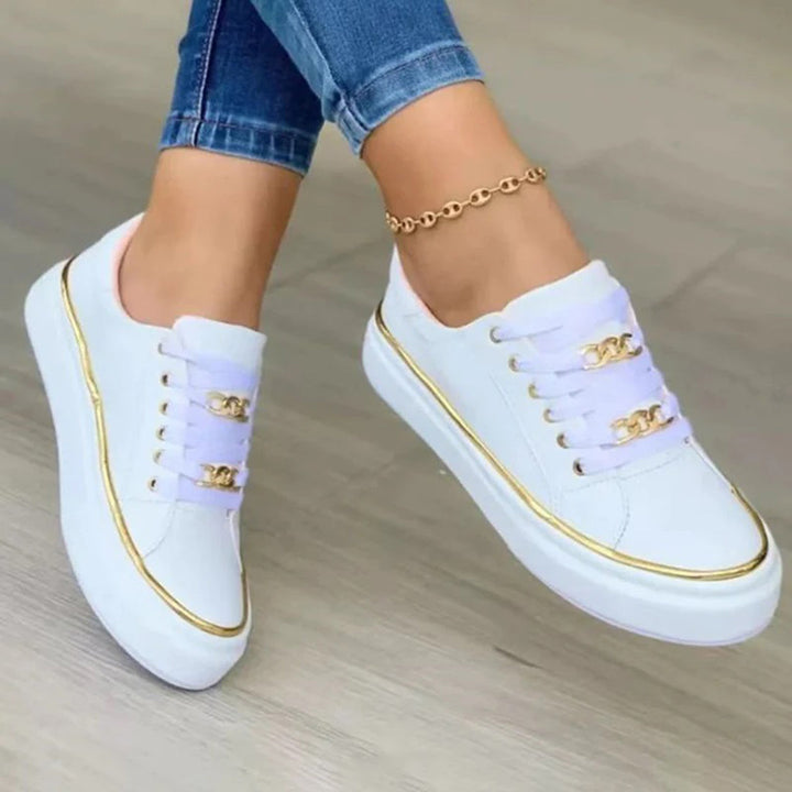 Witte stijlvolle damesschoenen met goudkleurige details aan de veters en zool