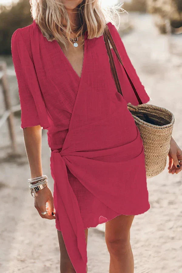 Korte damesjurk met wikkelstijl, trendy knoopdetail en V-hals, beschikbaar in diverse kleuren.