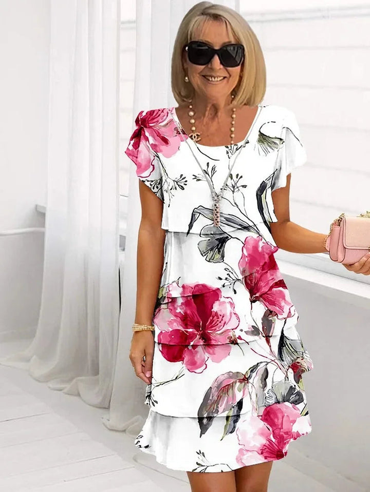 Vrolijke dame draagt een witte ruffle gelaagde mini jurk met roze bloemenprint, stralend in het daglicht.