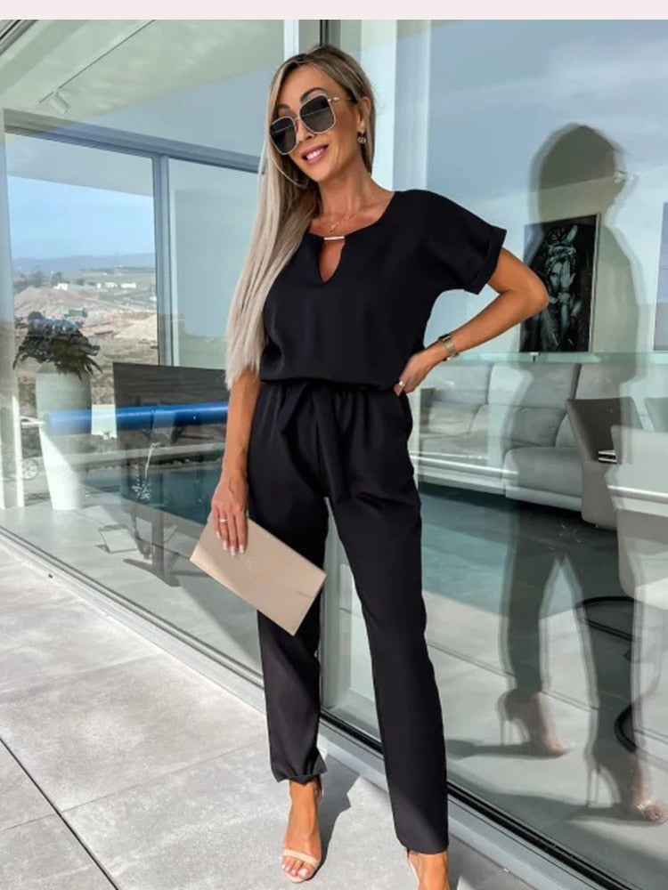 Elegante zwarte dames jumpsuit met korte mouw, V-hals en een subtiele strikceintuur, perfect voor avonden.