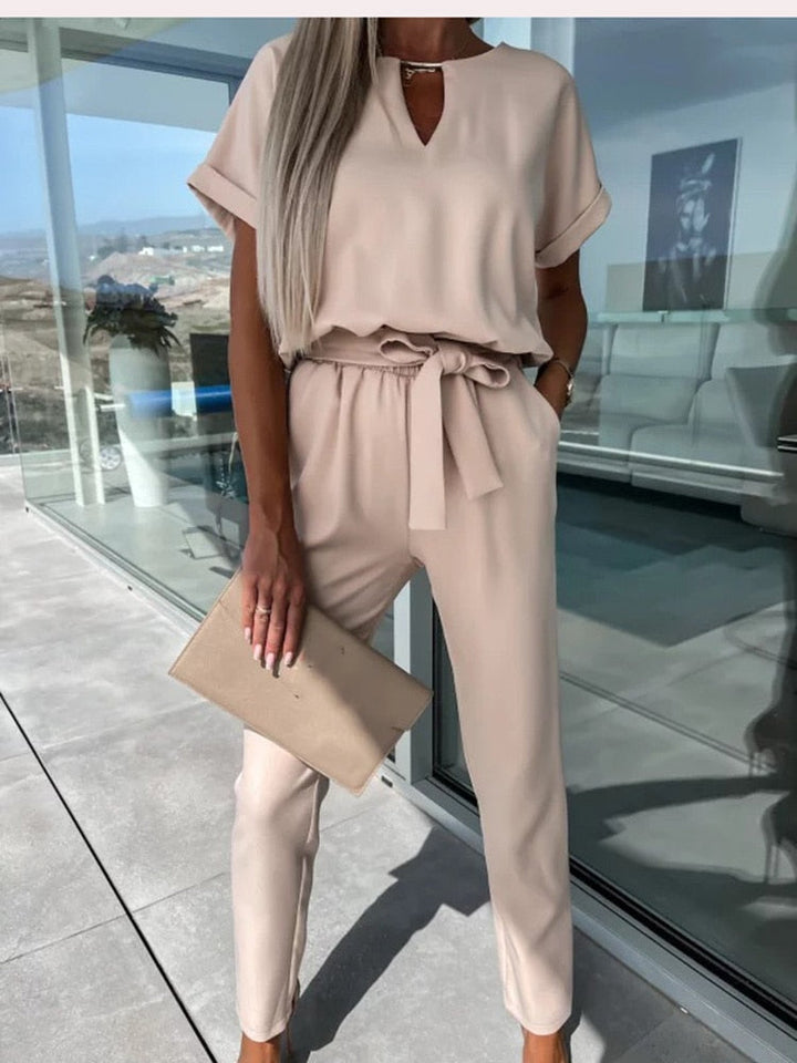 Modieuze rozenrode dameskleding: jumpsuit met korte mouw, diepe V-hals en een taille-accentuerende strikceintuur.