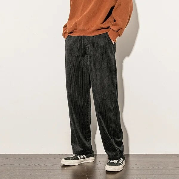 Man draagt zwarte corduroy broek Finn met oranje trui en sneakers