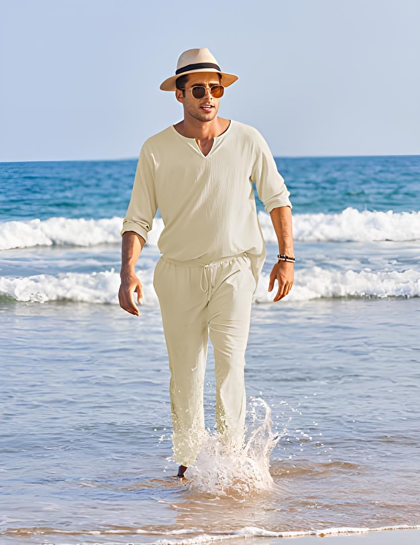 Stijlvolle man in een khaki 2-delige herenset met zonnebril en hoed, genietend van een zomerse dag aan zee.