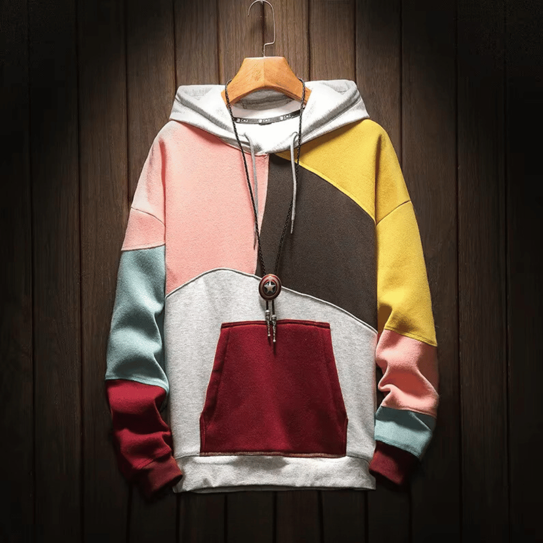 Heren hoodie met patchwork design in roze, grijze en gele tinten, hangend op een houten achtergrond.