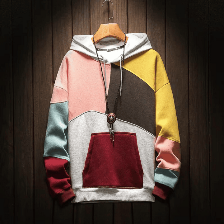 Heren hoodie met patchwork design in roze, grijze en gele tinten, hangend op een houten achtergrond.