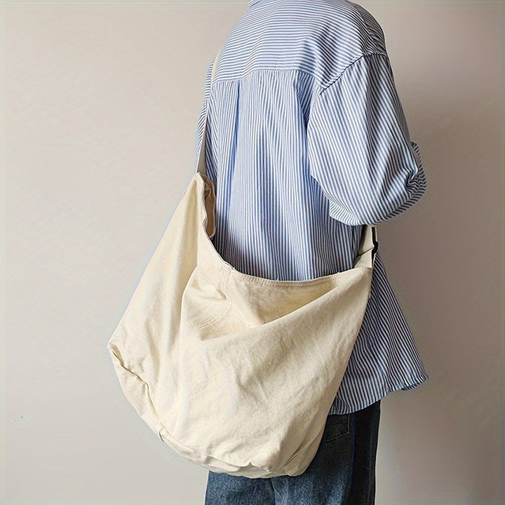 Man draagt een stijlvolle heren canvas schoudertas als crossbody, praktisch voor onderweg. Verstelbare riem.