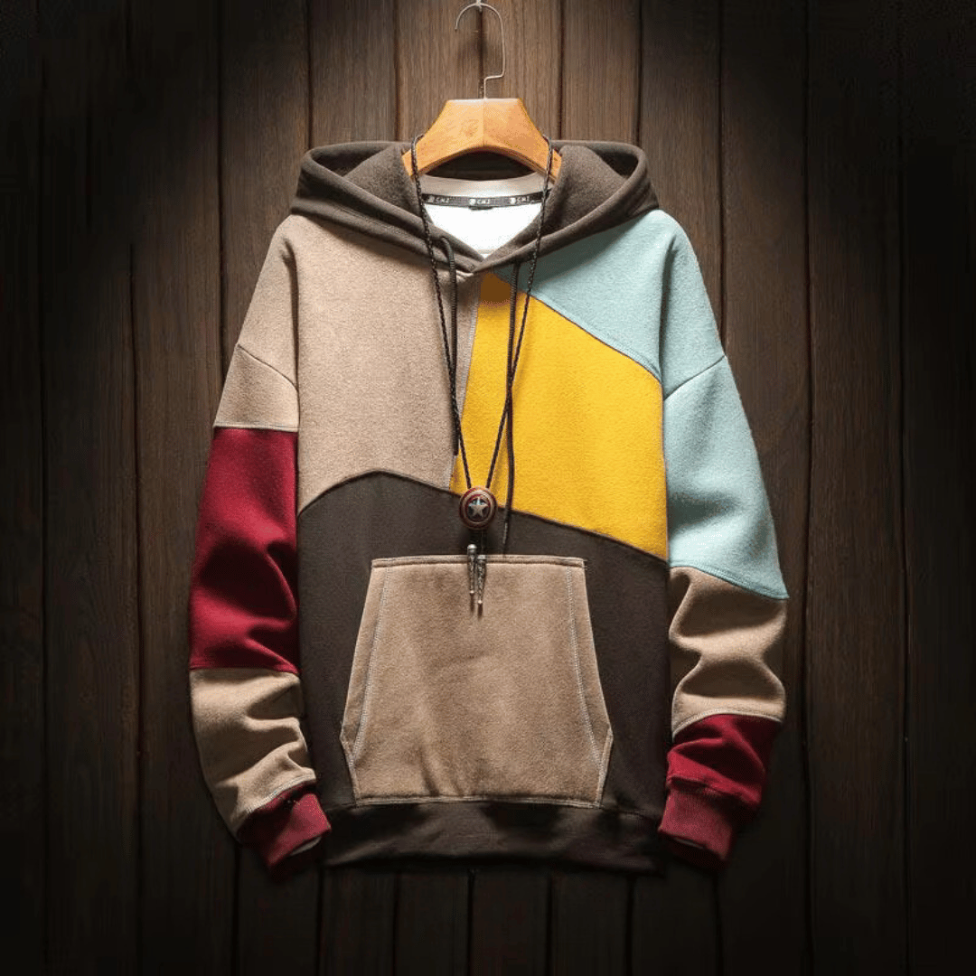 Heren hoodie met patchwork design in bruine, beige en gele tinten, hangend op een houten achtergrond.