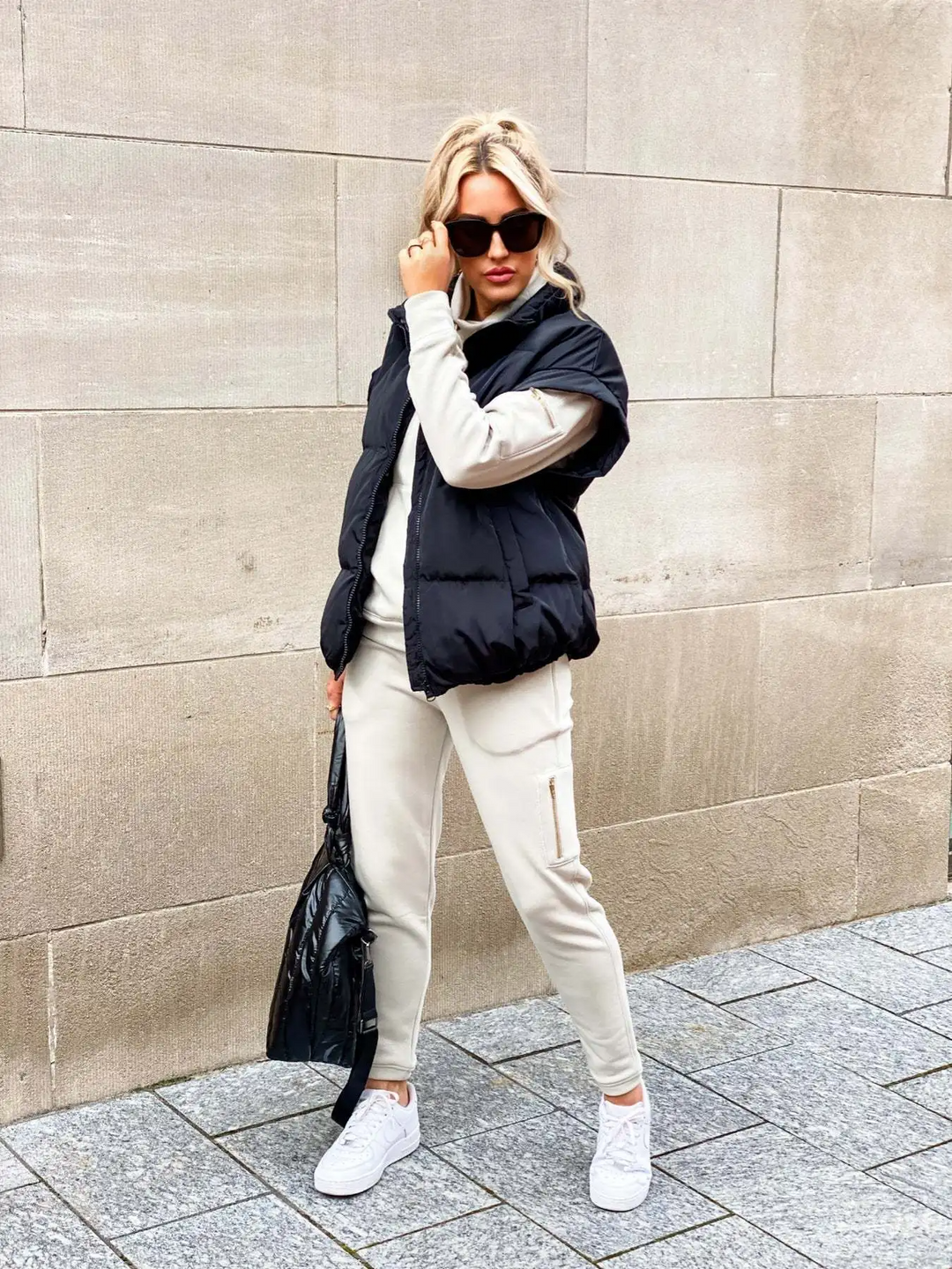 Dames draagt zwart puffer vest met zonnebril en lichte kleding