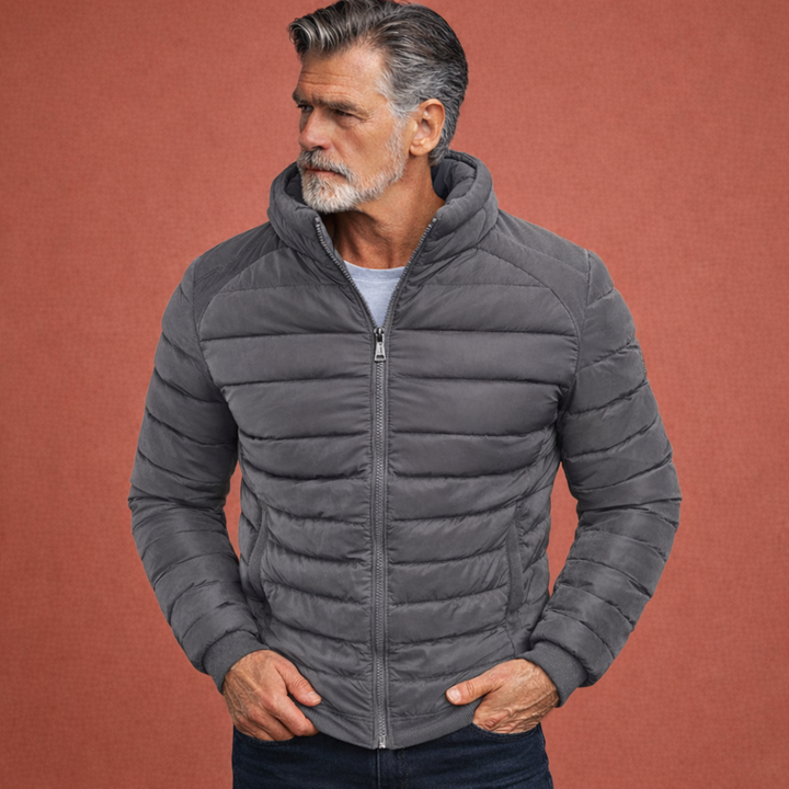 Model draagt casual heren gewatteerde jas met opstaande kraag. Stijlvolle overgangsjas met slanke pasvorm voor de man.