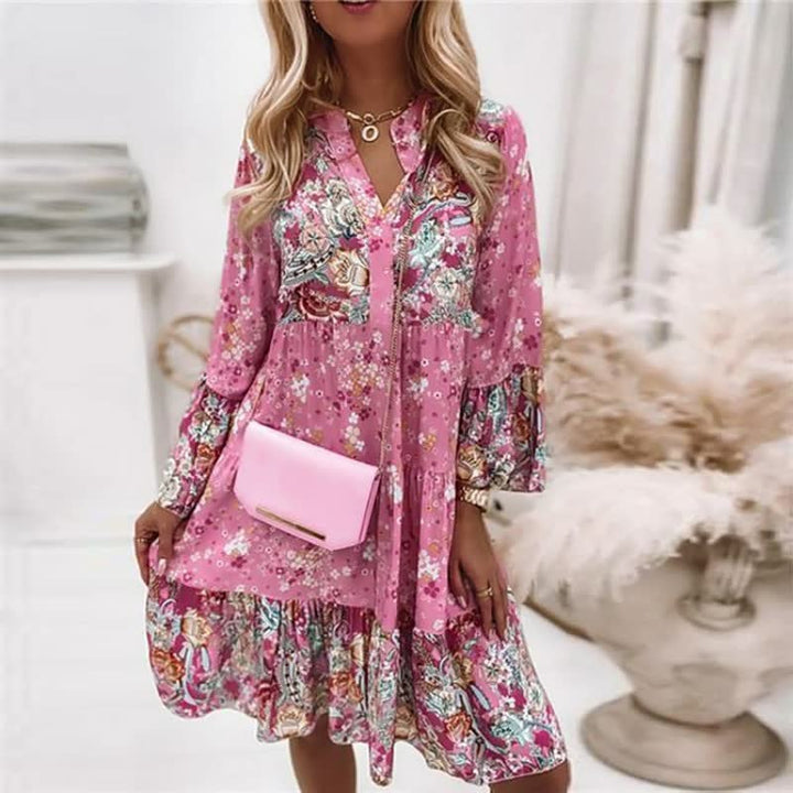 Vrouw draagt een roze boho jurk met bloemmotief, staand in een lichte kamer, stralend en comfortabel.