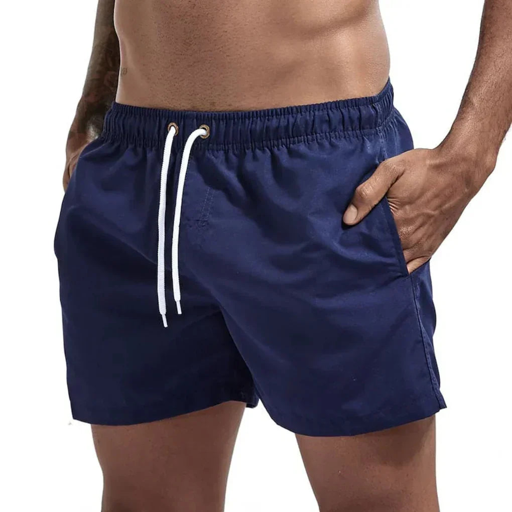 Relaxte man in sneldrogende heren zwemshorts, genietend van een welverdiende vakantie aan zee.